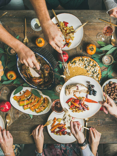 Flat-lay of friends feasting at Thanksgiving Day table with turkey, pumpkin pie, roasted seasonal vegetables and fruit, top view