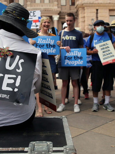 And group of demonstrators, one with a sign taped to their back saying "Let Us Vote!"