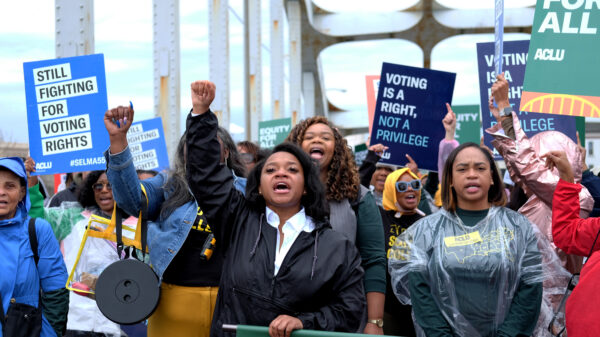 crowd marches with signs behind a banner while marching over the edmund pettus bridge
