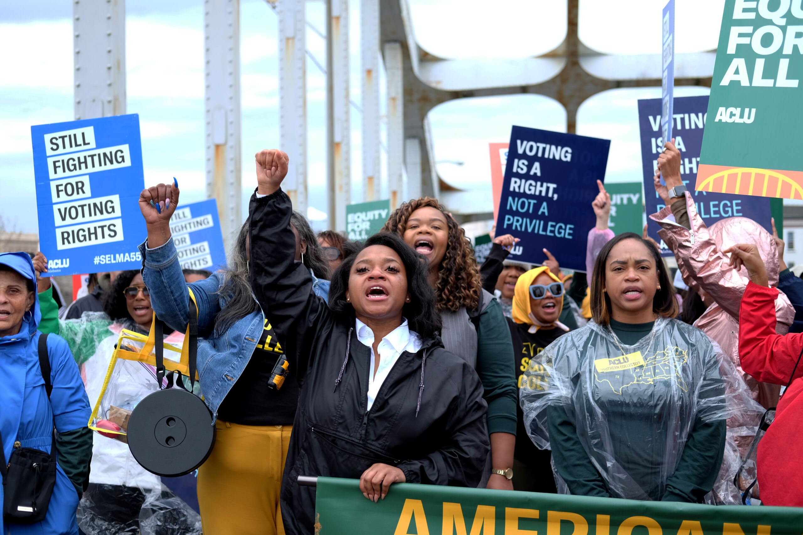 crowd marches with signs behind a banner while marching over the edmund pettus bridge