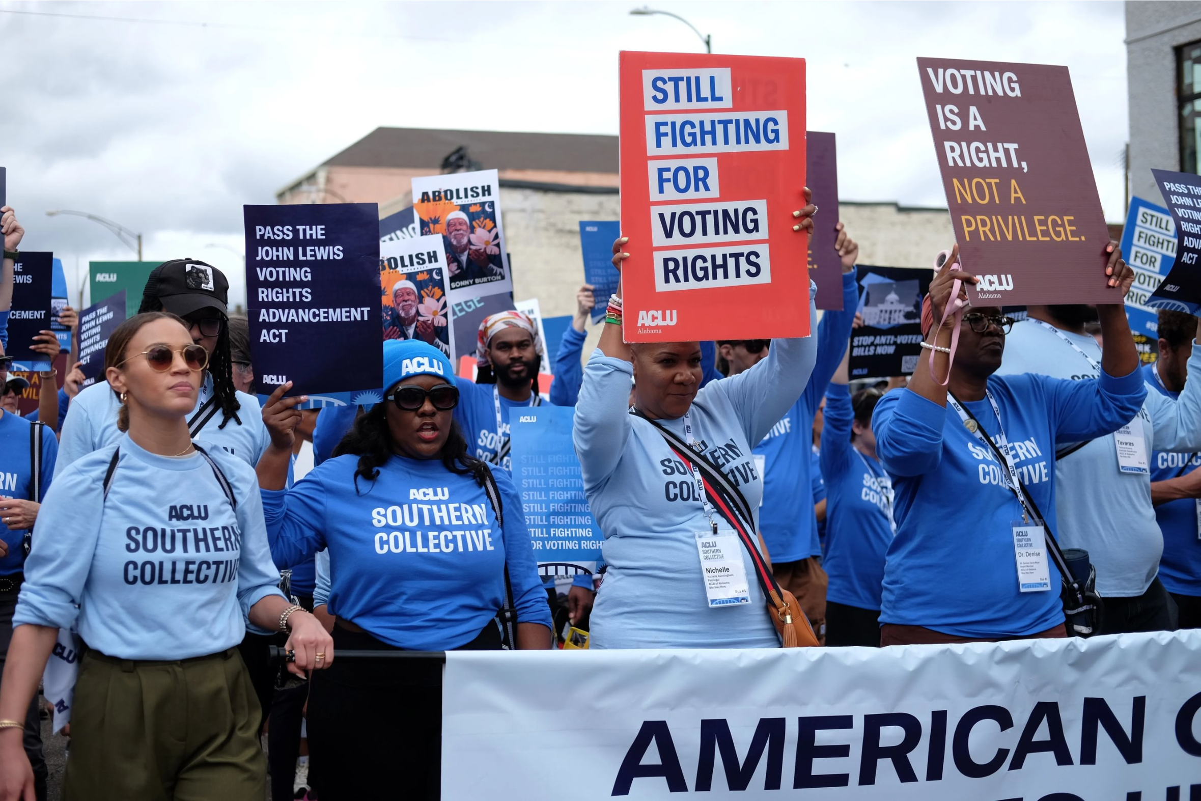 aclu members walk behind a banner carrying voting rights signs