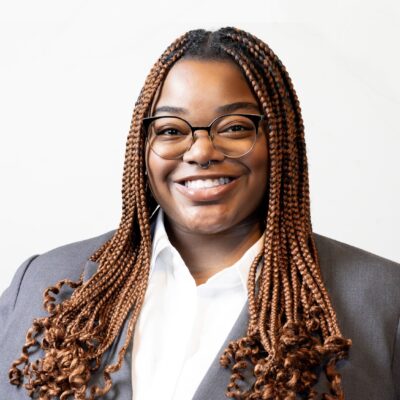 Black woman with glasses and long braids in a collared shirt and blazer