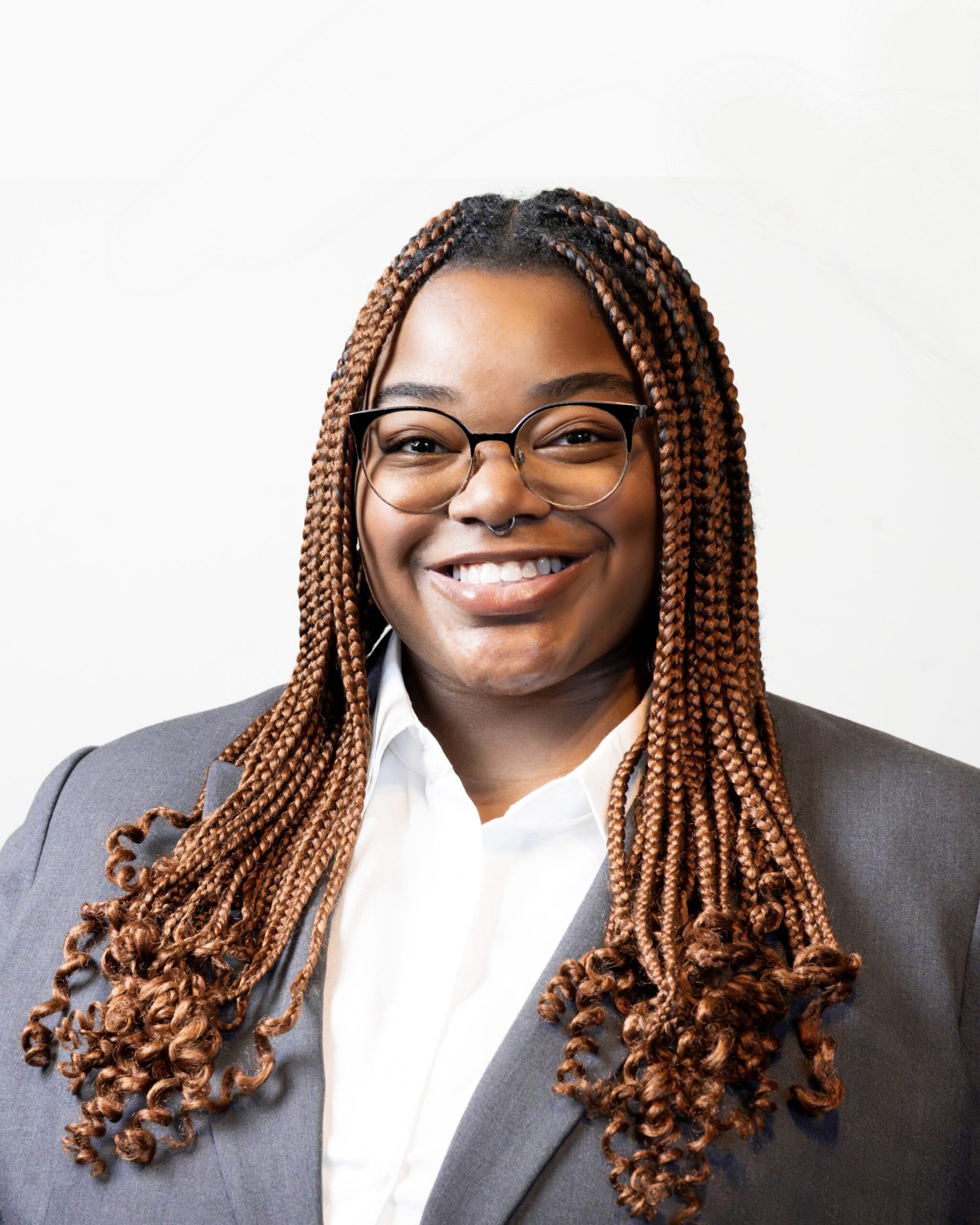 Black woman with glasses and long braids in a collared shirt and blazer
