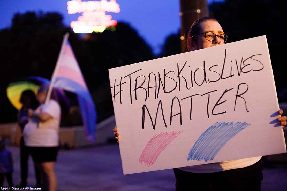 A transgender rights advocate holds a sign saying #TransKidsLivesMatter.