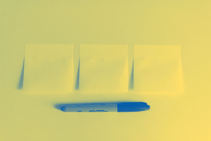 A photo of sticky notes on a table with a pen below.