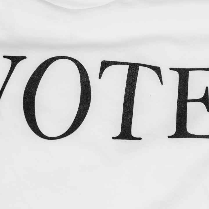 A photo of a white textured background with black text that reads "Vote". Photo was taken by Cyrus Crossan